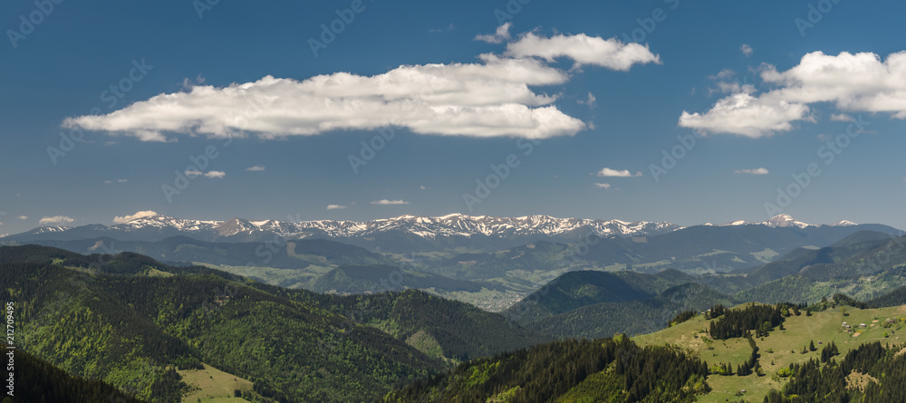 Scenic panoramic shot taken at sunny spring day. Mountains covered with forest and meadows, snowy mountains and blue sky with clouds. Concept of clear environment. Natural background. Scenic panoramic shot taken at sunny spring day. Mountains covered with forest and meadows, snowy mountains and blue sky with clouds. Concept of clear environment. Natural background.