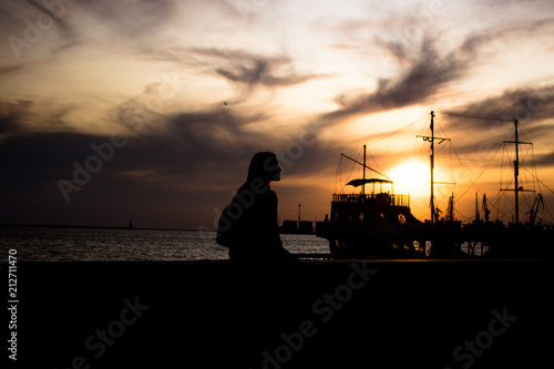 silhouette of a girl on the waterfront. silhouette of an old ship in the background. the girl is waiting for the ship photo