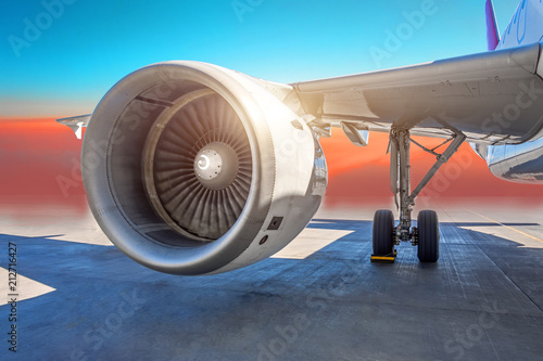 Aircraft jet engine close-up, airplane wing and chassis of landing gear wheel parked at the airport on a sky clouds background.