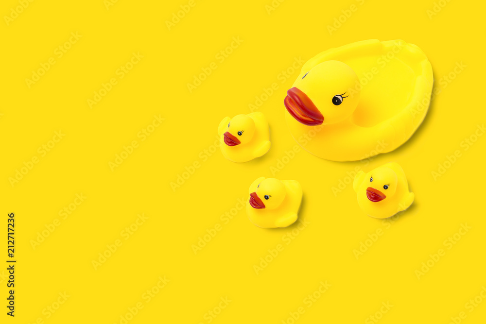 Rubber toy of yellow color Mama duck and small ducklings on a yellow background. The concept of maternal care and love for children. Flat lay, top view Rubber toy of yellow color Mama duck and small ducklings on a yellow background. The concept of maternal care and love for children. Flat lay, top view