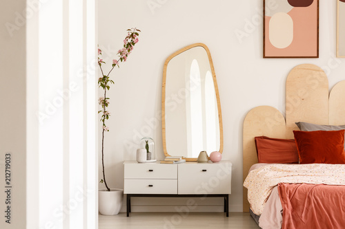 Fotografie Plant next to white dressing table with mirror in red bedroom interior with poster above bed