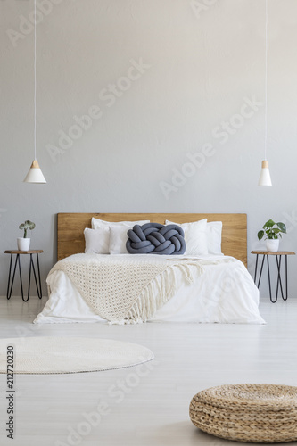 Pouf in spacious grey bedroom interior with lamps above bed with blue pillow. Real photo