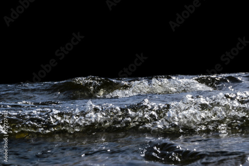 Big windy waves splashing over rocks. Wave splash in the lake isolated on black background. Waves breaking on a stony beach, forming a spray. Water splashes. Water surface texture