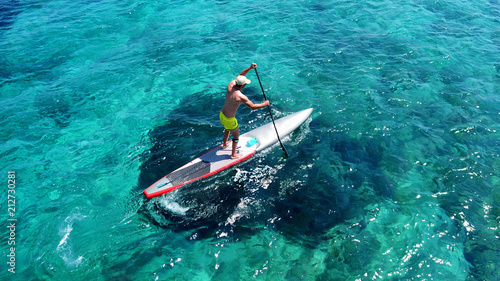 Aerial drone bird's eye view of fit man exercising sup board in turquoise tropical clear waters
