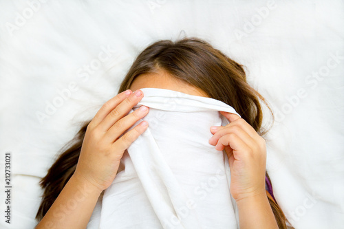 a girl with blue eyes hiding behind a sheet