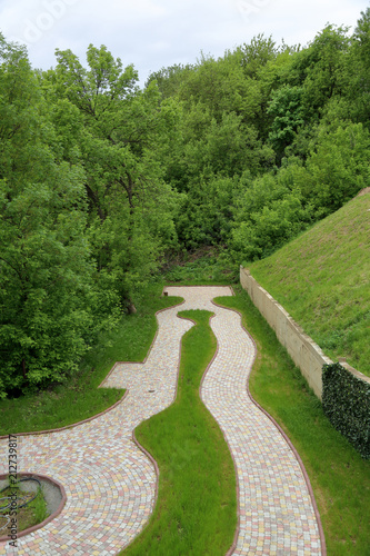 A winding path for walks from stone tiles among trees and a green lawn  