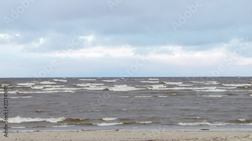 Sea coastal waves rolling on empty sandy beach, stormy cloudy sunrise skyview. Video. Sea waves on sandy beach. Seascape with grey water on cloudy sky. Power of nature. Wanderlust or travelling and photo