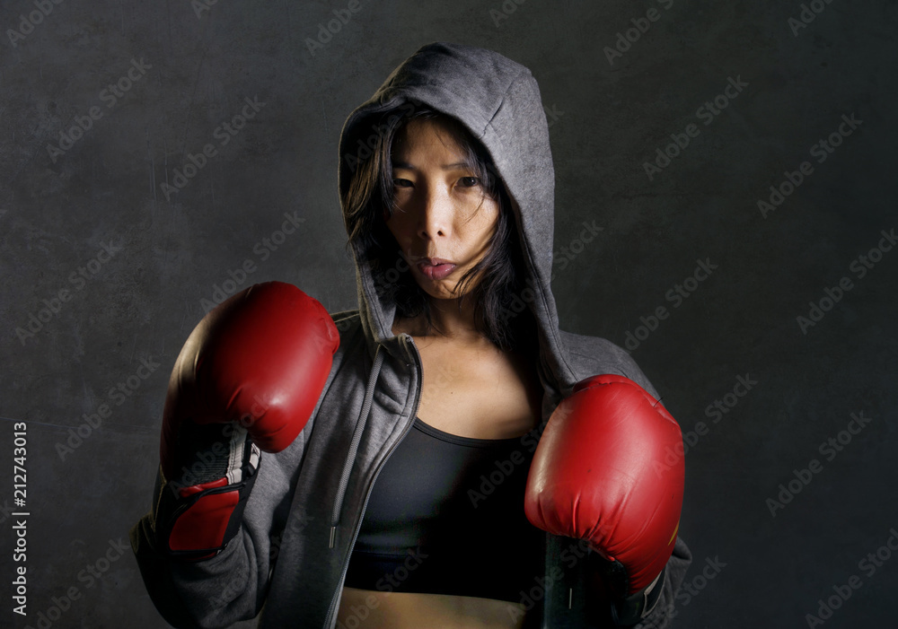 close up portrait of young fit and healthy Asian Chinese boxer woman in fitness top hoodie and boxing gloves posing cool badass attitude angry close up portrait of young fit and healthy Asian Chinese boxer woman in fitness top hoodie and boxing gloves posing cool badass attitude angry