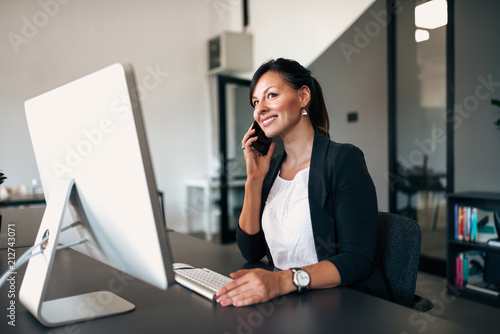 Businesswoman making call while sitting at office in front of computer.
