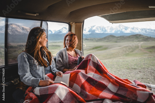 two young girls sitting in the van and talking with each other. beautiful mountain valley on the background.