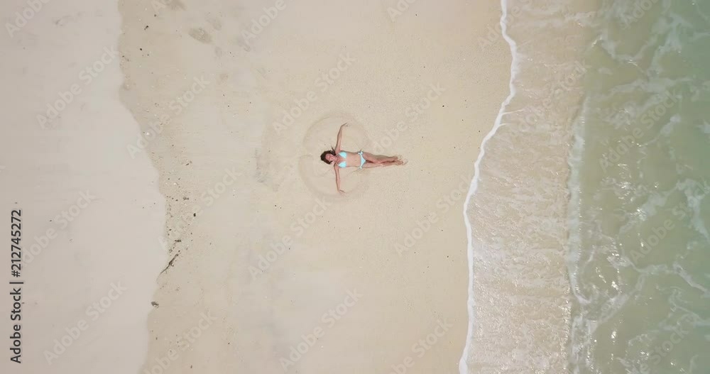 Camera moving up from beautiful girl lying on the white sand beach with ...