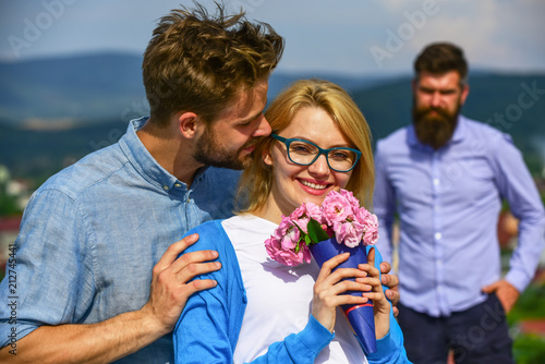 Couple in love dating while jealous bearded man watching wife cheating him with lover. Couple romantic date lovers bouquet flowers. Infidelity concept. Lovers hugs outdoor flirt romance relations photo