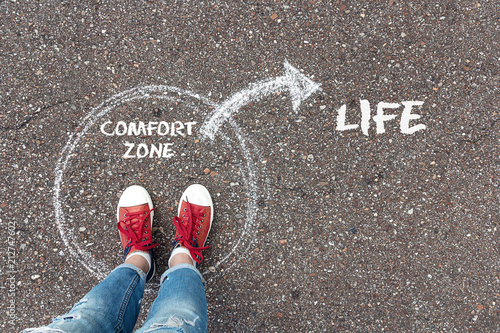 Exit from the comfort zone concept. Feet standing inside circle comfort zone and outward arrow chalky on the asphalt.