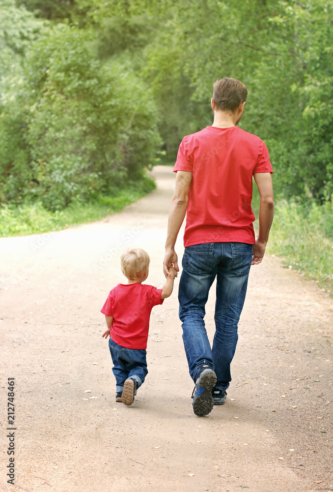 Father and his toddler boy are walking in the park, holding hands. Fatherhood concept. Family look clothing Father and his toddler boy are walking in the park, holding hands. Fatherhood concept. Family look clothing