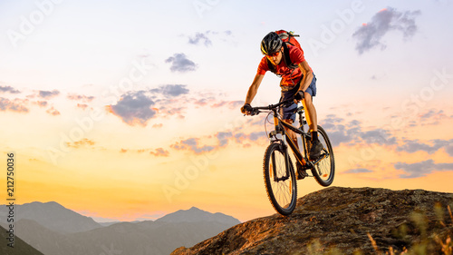 Fototapeta Naklejka Na Ścianę i Meble -  Cyclist in Red Riding the Bike Down the Rock at Sunset. Extreme Sport and Enduro Biking Concept.