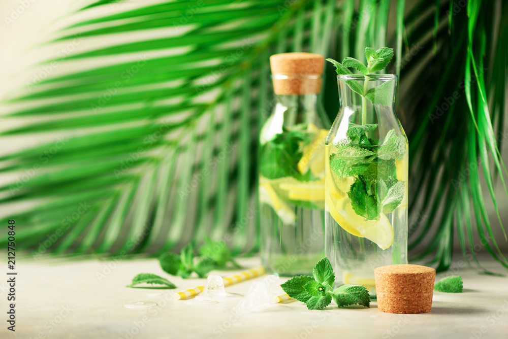 Bottle of detox water with mint, lemon, tropical palm leaves on grey background. Citrus lemonade. Summer fruit infused water. Copy space. Bottle of detox water with mint, lemon, tropical palm leaves on grey background. Citrus lemonade. Summer fruit infused water. Copy space.