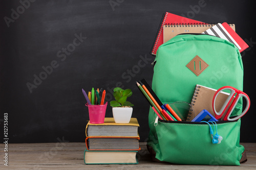 Education concept - school backpack with books and other supplies, blackboard background