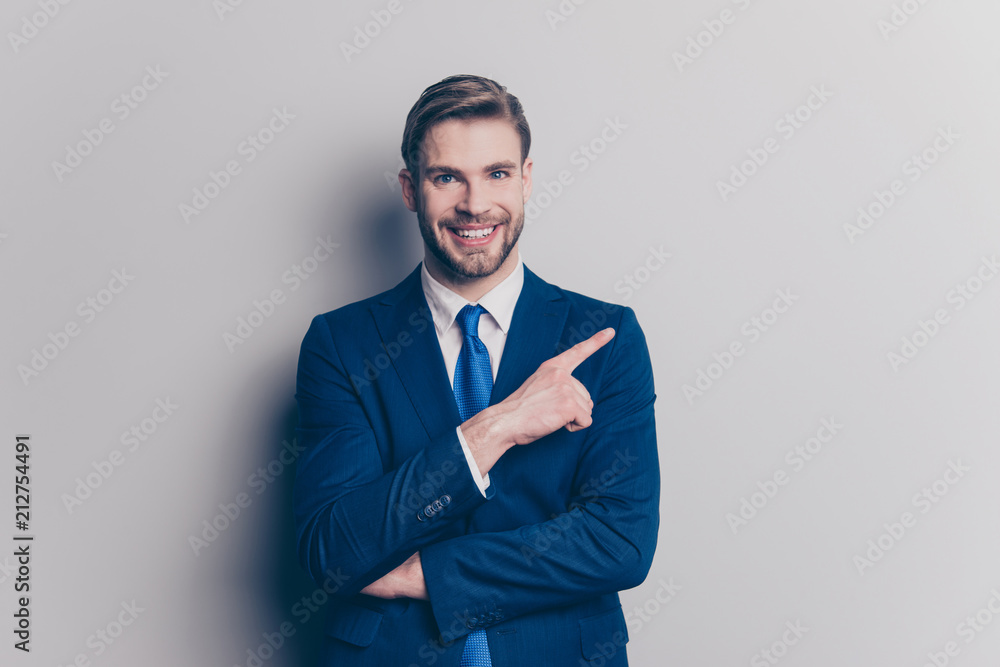 Portrait with copy space for advertisement, product of cheerful, positive, trendy man with hairstyle, stubble showing with forefinger empty place, isolated on grey background, looking at camera - obrazy, fototapety, plakaty 