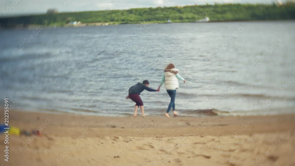 The mother plays with her son in a raincoat and runs down the sea at the beach The mother plays with her son in a raincoat and runs down the sea at the beach