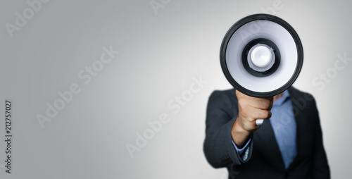 announcement - businessman with megaphone in front of face on gray background photo