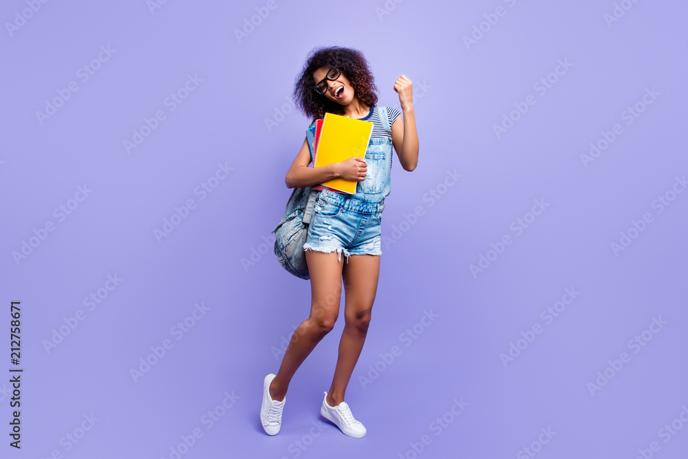 Full size portrait of glad successful girl in jeans overall sneakers denim outfit celebrating pass exams holding textbooks isolated on violent background highschool high school Full size portrait of glad successful girl in jeans overall sneakers denim outfit celebrating pass exams holding textbooks isolated on violent background highschool high school