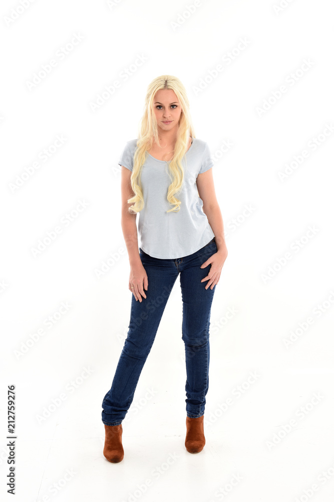 Fototapeta premium full length portrait of blonde girl wearing blue shirt and jeans, standing pose isolated on white studio background.