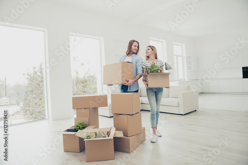 Joy credit person just married delivery furniture window concept. Cheerful tender glad joyful beautiful lovely people in jeans holding opening carton packages with stuff looking at each other © deagreez