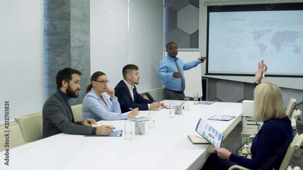 African businessman using remote and giving presentation to multi-ethnic team of colleagues at corporate meeting African businessman using remote and giving presentation to multi-ethnic team of colleagues at corporate meeting