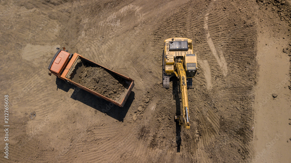 Aerial photo of excavator pours sand into the truck. On the construction site top view. Shooting from the drone/