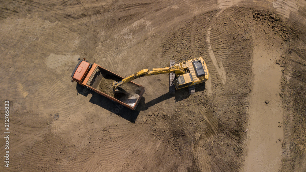 Aerial photo of excavator pours sand into the truck. On the construction site top view. Shooting from the drone/ Aerial photo of excavator pours sand into the truck. On the construction site top view. Shooting from the drone/