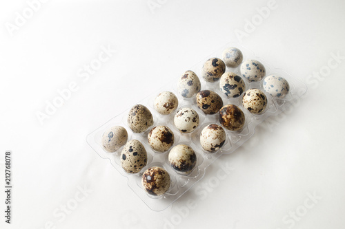 Fresh quail eggs in a plastic tray on a white background