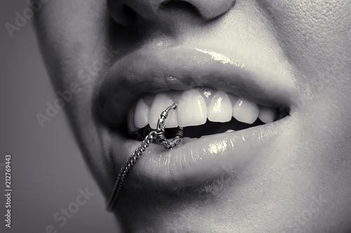 Accessories. Woman with piercing in mouth. Open lips with metal ring between teeth. Fun expression or grimace on beautiful face of attractive girl. Modern lifestyle and piercing trends in young people © Tverdokhlib