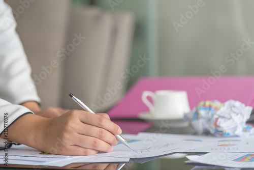 Businesswomen review graph of annual sales with paper garbag, cup of coffee, files and mobile phone as a blurred background. Sale women seriously make a sale plan for next year. photo