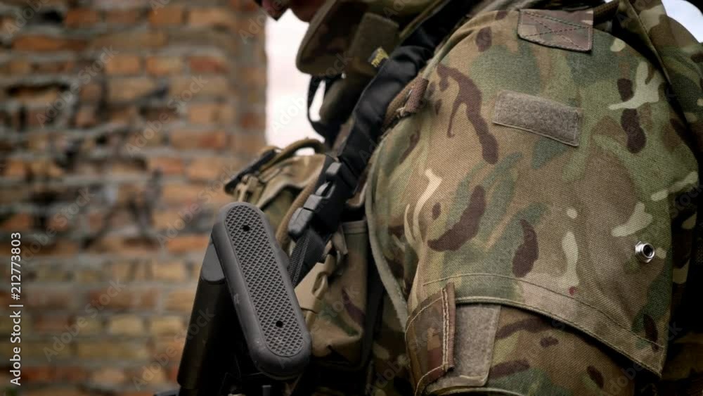 Part of armed soldier with ammunition and weapon, standing nea brick wall background, war concept Part of armed soldier with ammunition and weapon, standing nea brick wall background, war concept