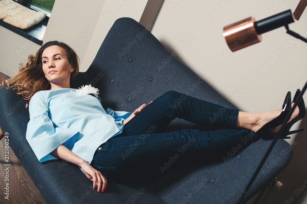 Stylish business woman taking a break. Attractive young woman lying on grey  sofa in a modern