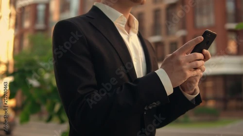 Guy is typing a message on a black celly. He wears black suit. photo