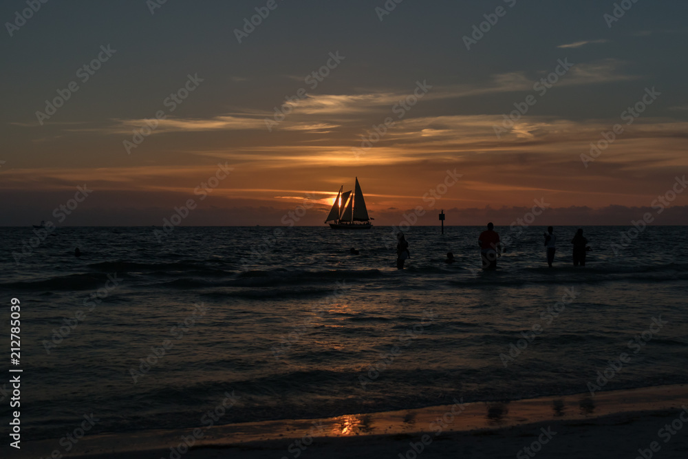 Silhouettes of sailboat and people on the horizon at sunset on the beach