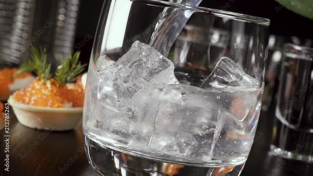 Slow motion in a glass of vodka and ice pour a soda near the appetizer with red caviar Slow motion in a glass of vodka and ice pour a soda near the appetizer with red caviar
