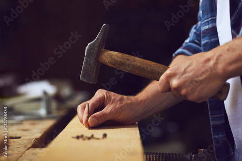 Slika na platnu Carpenter hammering a nail into wooden plank in a carpentry shop