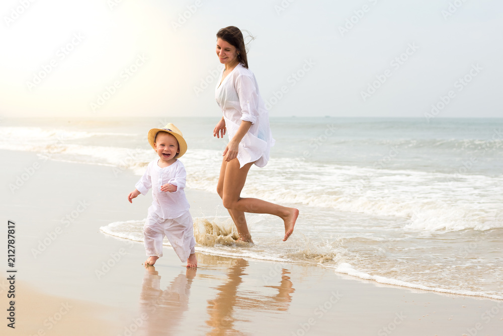 Young beautiful girl in white shirt with little boy in white clothes running on sea water and smiling cheerfully