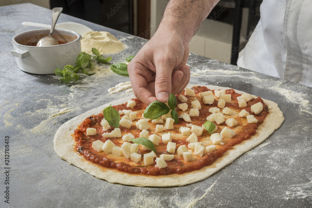 Basil leaves over freshly prepared Pizza Margherita. Basil garnish to flavor a unbaked Pizza