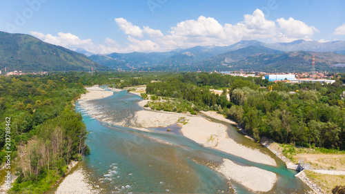 Aerial view, braided river flowing between woodland with mountain background and cloudscape, Turin, Italy
