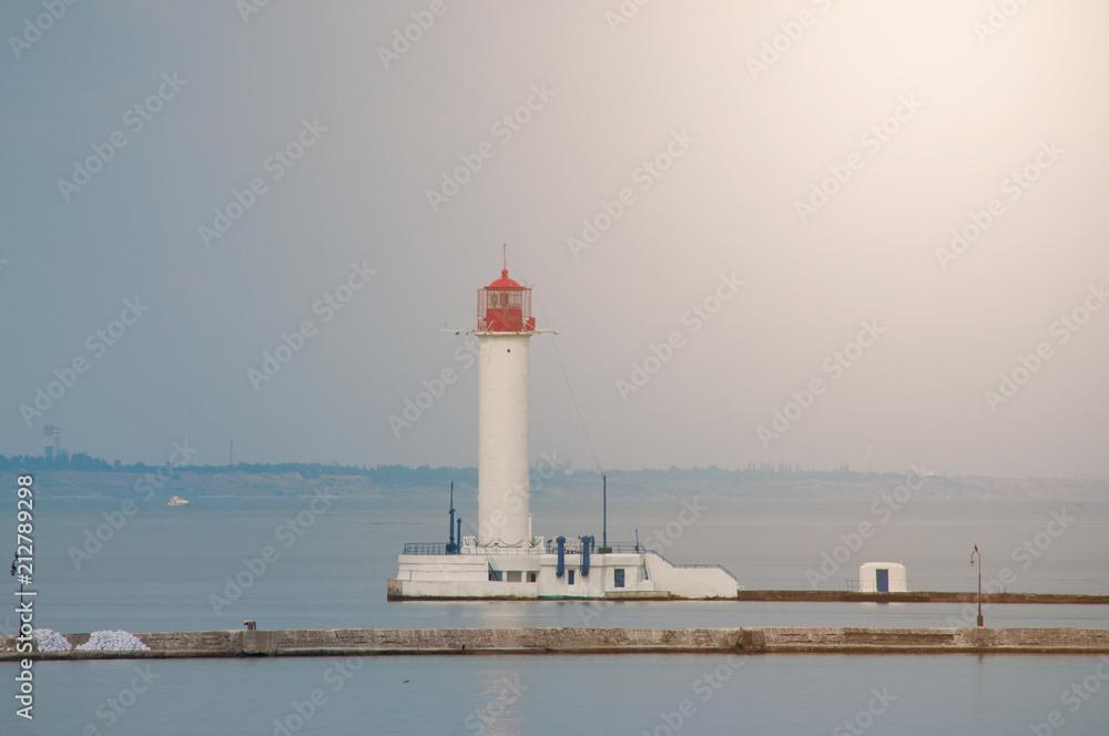 Summer seascape with a white lighthouse with red top in the middle. Calm sunny day