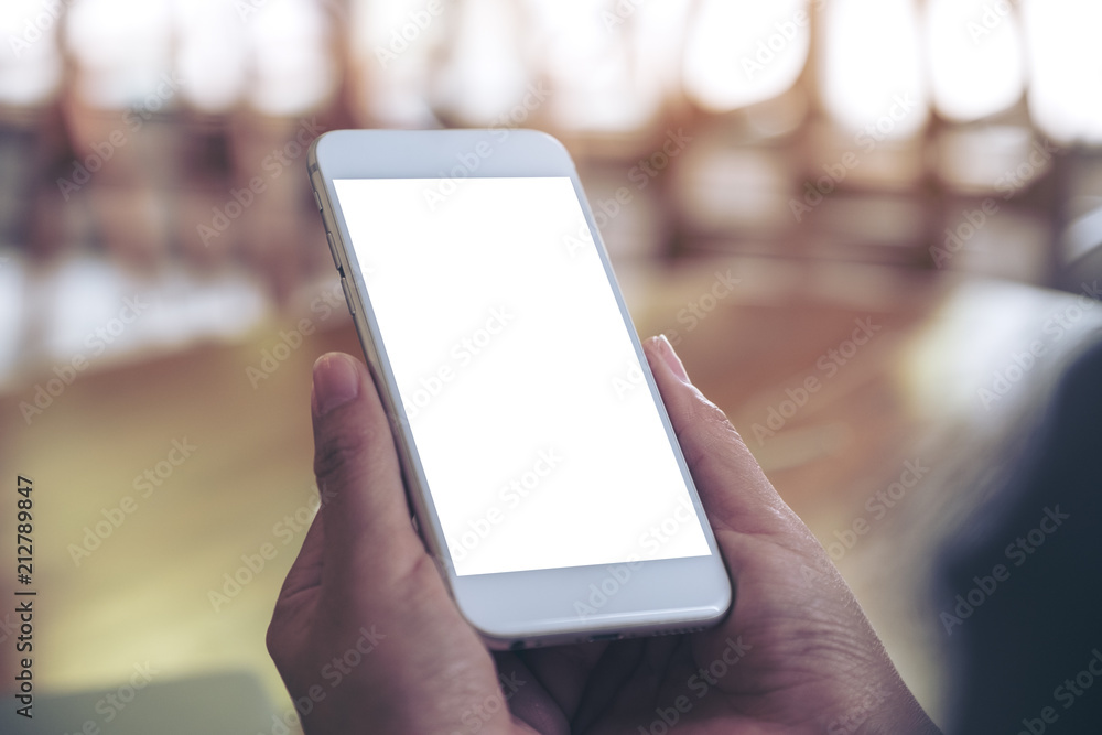 Mockup image of hands holding white mobile phone with blank desktop screen with blur background