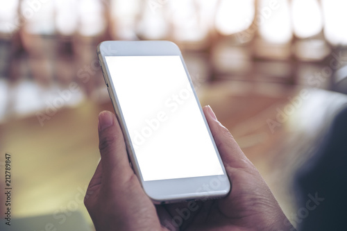 Mockup image of hands holding white mobile phone with blank desktop screen with blur background