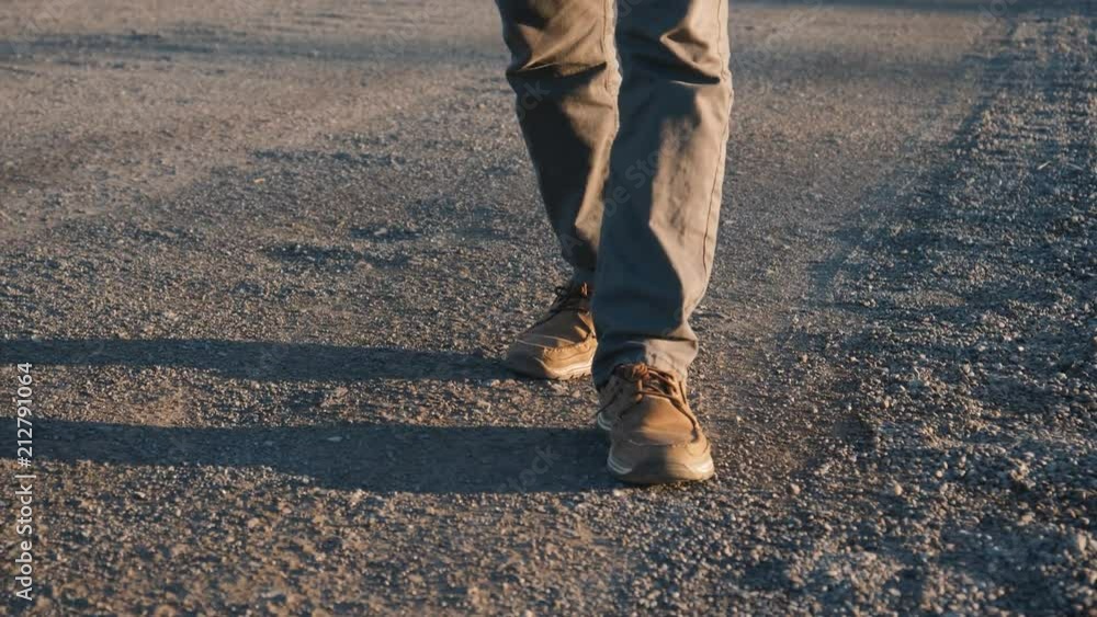 Feets of a male worker walking on a gravel road at sunset after a day at work. Feets of a male worker walking on a gravel road at sunset after a day at work.
