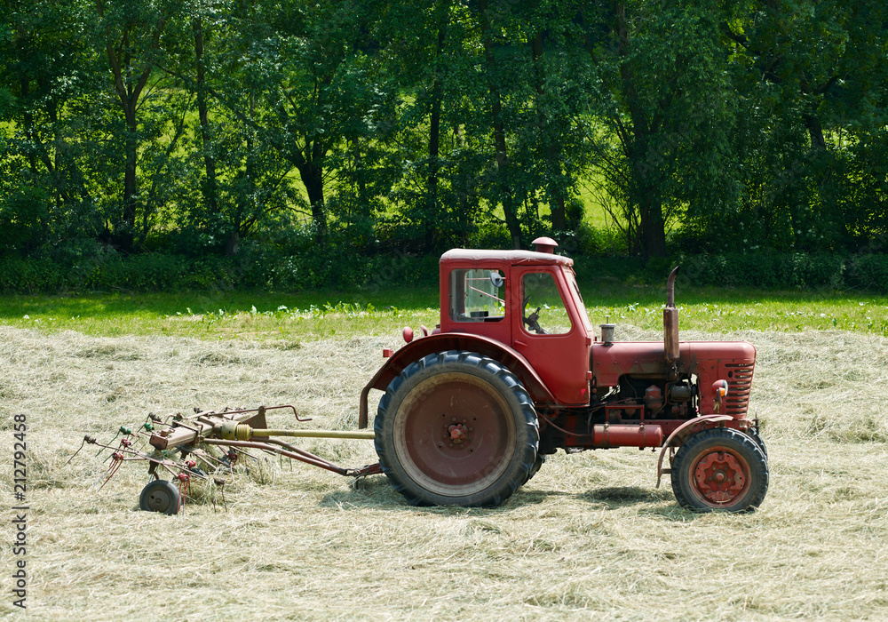 Brahmenau / Germany: Old but robust red tractor from socialist times with rotary hay tedder on a small field in June Brahmenau / Germany: Old but robust red tractor from socialist times with rotary hay tedder on a small field in June