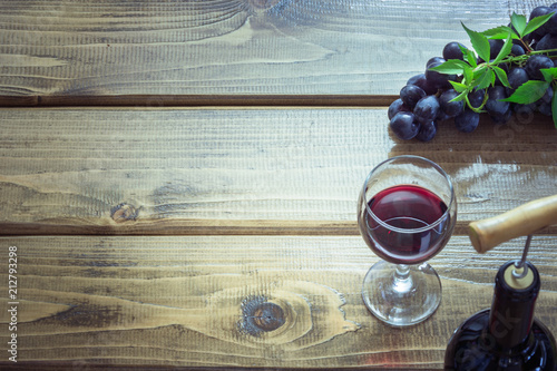 Open bottle of red wine with wineglass, corkscrew and ripe grape on wooden board. Copy space and top view.