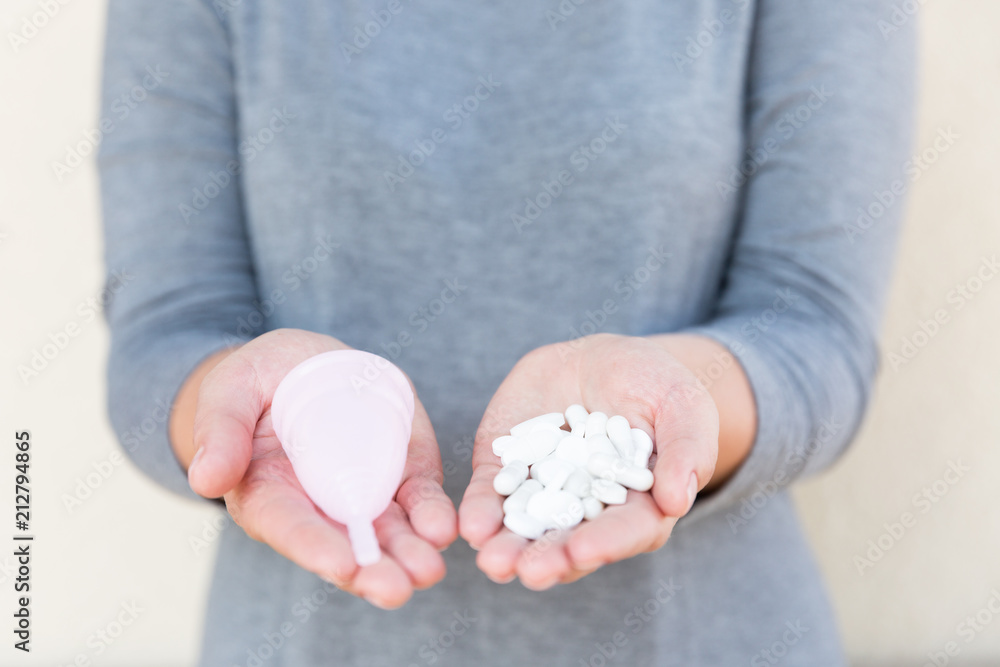 Tablets or Menstrual cup? Menstrual mug and tablets holds a female hand. Tablets or Menstrual cup? Menstrual mug and tablets holds a female hand.