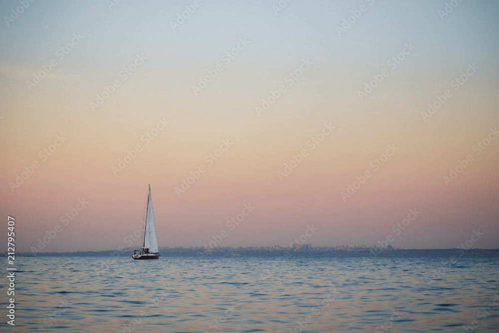 Nice view of small white sailboat, yacht sailing at sunset